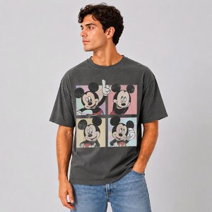 Puede incluir: Una camiseta de manga corta en color gris carb&oacute;n con un estampado gr&aacute;fico de Mickey Mouse en cuatro poses distintas, cada una dentro de un marco cuadrado con un fondo de color pastel diferente, incluyendo verde claro, rosa, amarillo y azul claro.
