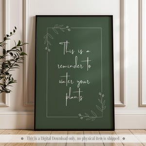 Peut inclure: Une impression d'art mural imprimable avec un fond vert et du texte blanc qui dit "Ceci est un rappel pour arroser vos plantes". Le texte est entouré d'un motif floral blanc.