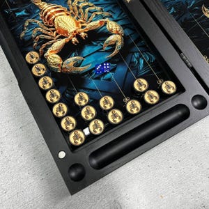 May include: Backgammon board with a gold scorpion design. The board is black with a blue and teal background. The game pieces are gold with a scorpion emblem. Two blue dice are visible.