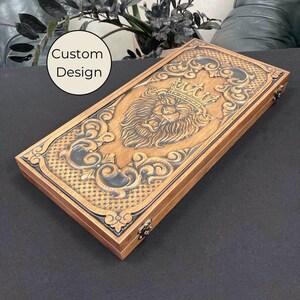 May include: A wooden game box with a carved lion head design and a gold crown. The box has a dark brown stain and a black background.