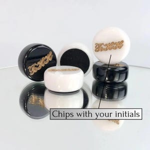 May include: Black and white game chips with gold lettering. The chips have the initials "T.H." on them. The text "Chips with your initials" is on the image.