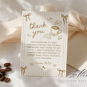 Puede incluir: Una tarjeta de agradecimiento rectangular con texto en tono dorado e ilustraciones de lazos, una taza de café, un cruasán y un chupete. La tarjeta dice: thank you FOR CELEBRATING MY BABY SHOWER WITH ME! YOUR PRESENCE AND WISHES TRULY MADE THE DAY SPECIAL.