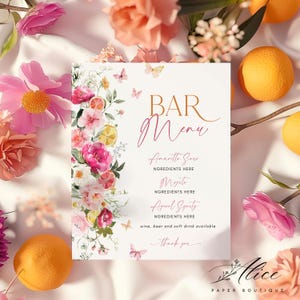 May include: A bar menu with the words "BAR Menu" in a stylish font. The menu features drink options like "Amaritto Sour" and "Mojito", with a floral design of pink flowers, butterflies, and citrus fruits. Oranges and flowers surround the menu.