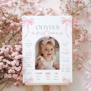 May include: A pink and white first birthday milestone poster with a photo of a baby girl. The poster includes the baby's name, Olivia, and details about her first year, including her weight, height, and milestones. The poster is decorated with pink bows.