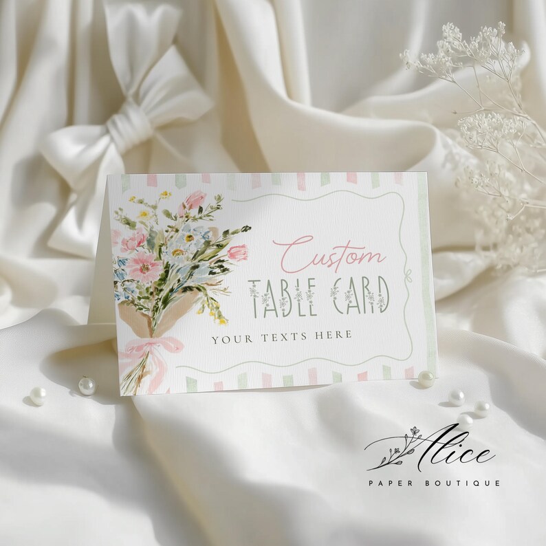 May include: A custom table card with a floral bouquet design. The card features the text "Custom Table Card" and "Your Texts Here". The bouquet includes pink, blue, and white flowers tied with a pink ribbon. The card is set against a white background.