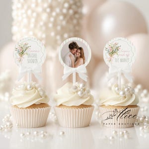 May include: Three cupcakes with white frosting and pearl decorations. Each cupcake has a decorative topper with text and a bow. One topper has a photo of a couple. The text on the toppers reads "Maria's Bridal Shower" and "Vivian's fresh off the market".