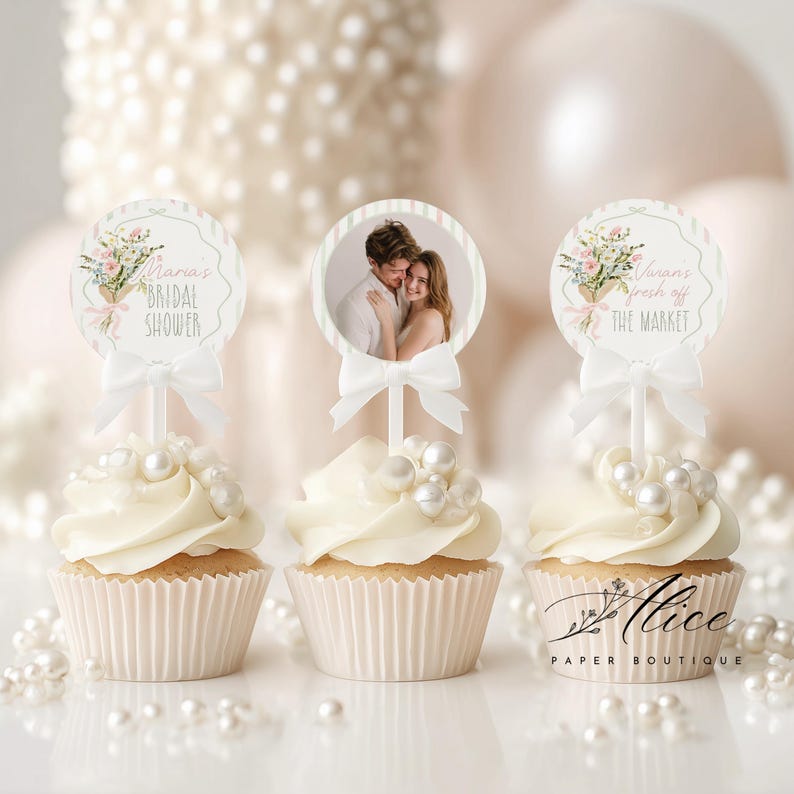 May include: Three cupcakes with white frosting and pearl decorations. Each cupcake has a decorative topper with text and a bow. One topper has a photo of a couple. The text on the toppers reads "Maria's Bridal Shower" and "Vivian's fresh off the market".