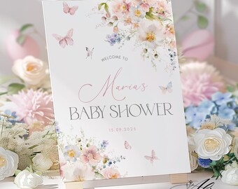 Może przedstawiać: Biały szyld na baby shower z kwiatowymi i motylkowymi akcentami. Na szyldzie widnieje napis "Witamy na Baby Shower Marii" z datą 15.09.2025. Szyld jest podparty drewnianym sztalugą. Szyld otoczony jest kwiatami.