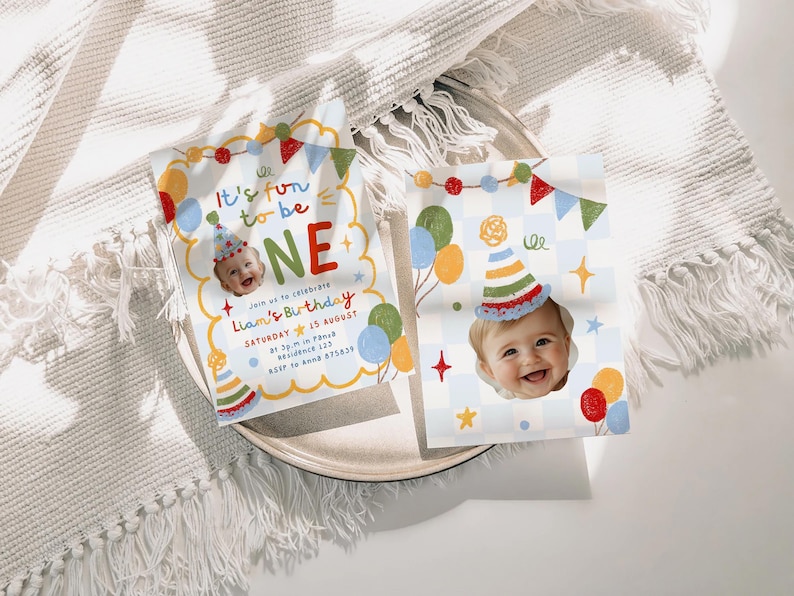 May include: Two rectangular birthday invitation cards featuring a photo of a baby wearing a party hat. The cards display colorful illustrations of balloons, bunting, and the text It's fun to be ONE, Join us to celebrate Liam's Birthday, Saturday 15 August.