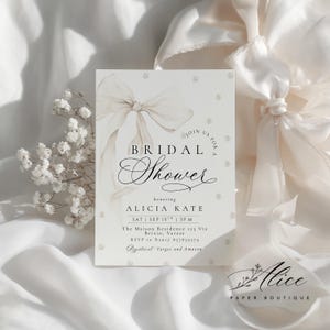 K&ouml;nnte beinhalten: Eine Einladung zur Brautparty in sanften, neutralen Farben. Das Design zeigt eine Aquarellschleife, Perlenakzente und elegante Schrift. Die Einladung enth&auml;lt den Text "BRIDAL Shower" und Details f&uuml;r Alicias Party.