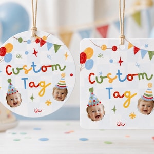 May include: Two hanging gift tags, one circular and one square, featuring a light blue checkered pattern. Each tag displays the text Custom Tag in colorful letters, decorated with party balloons, bunting, stars, and photos of a smiling baby.