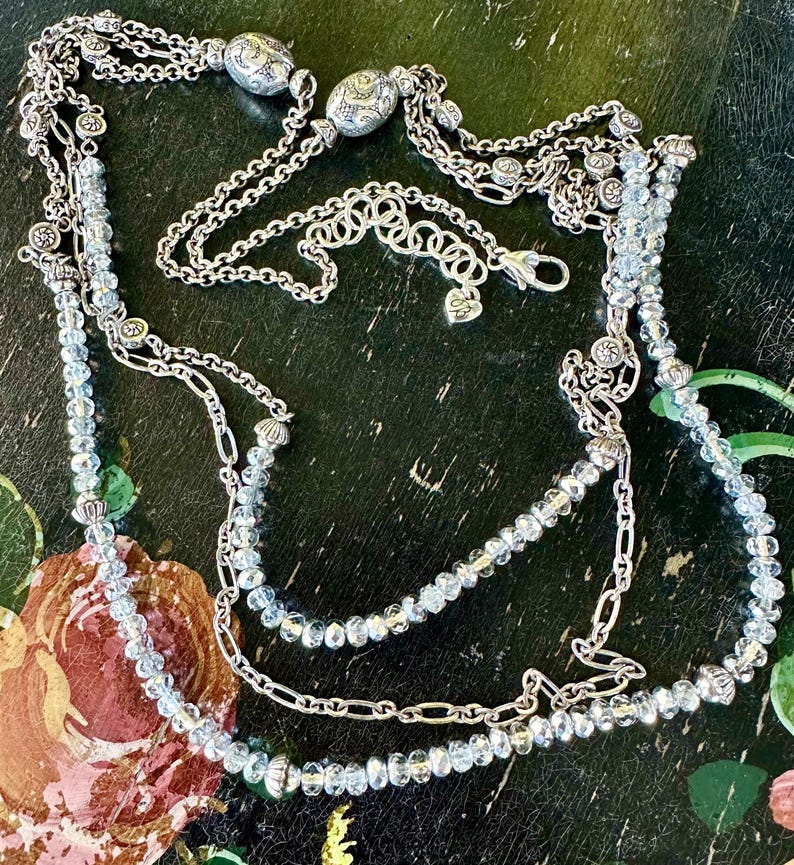 May include: A multi-strand necklace with silver-toned chains and light blue crystal beads. The necklace features decorative silver accents and a lobster clasp closure. The design includes multiple layers of chains and beaded strands.