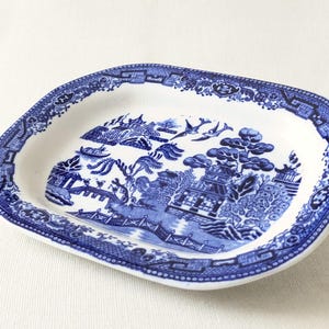 May include: Oval-shaped, white and blue ceramic dish with a Willow pattern design. The blue pattern features a landscape with pagodas, bridges, and trees. The rim has a detailed blue border. A classic piece for serving or display.