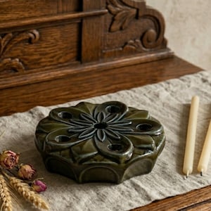 May include: A dark green ceramic candle holder with a floral design. The holder has multiple openings for candles and is surrounded by two lit candles. Dried flowers and wheat stalks are on the left.