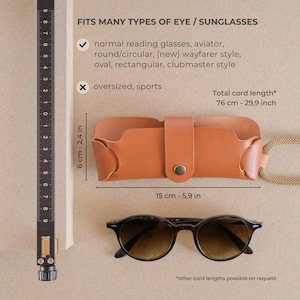May include: A brown leather glasses case with a snap closure and a cord for carrying. The case measures 6 cm by 15 cm. The text on the image reads "Fits many types of eye/sunglasses" and lists the types of glasses the case fits. The text also says "Total cord length* 76 cm - 29.9 inch" and "*other cord lengths possible on request".