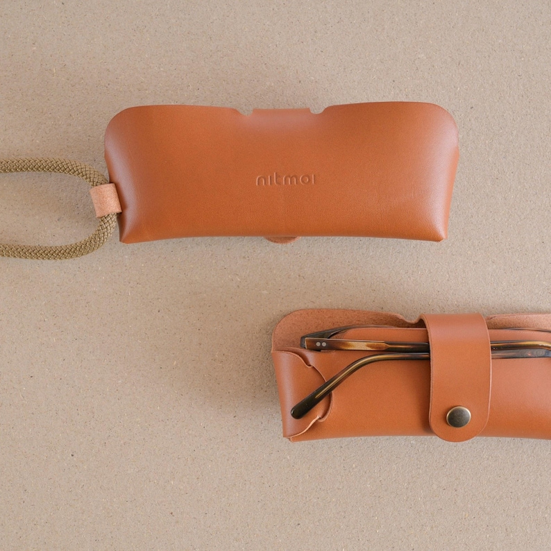 May include: A brown leather glasses case with a strap and the word "nitmol" embossed on the front. The case is open and a pair of brown glasses is inside.