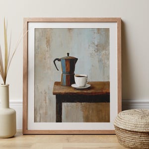 May include: Framed art print depicting a coffee pot and a cup of coffee on a wooden table. The coffee pot is blue and brown, and the cup is white. The background has a textured, neutral colour.