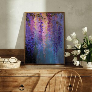 May include: A framed painting depicting wisteria flowers in purple, pink, and blue hues. The artwork is placed on a wooden chest of drawers, with a basket and a vase of white tulips. The painting has a wooden frame.