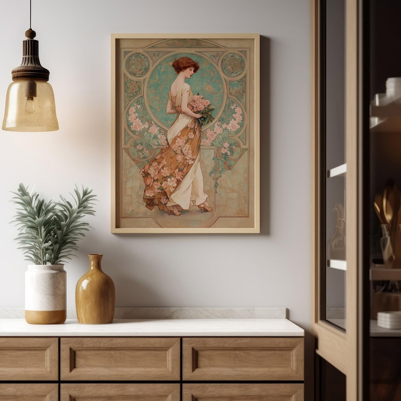 May include: A framed art print featuring a woman in a flowing gown, holding a bouquet of pink flowers. The artwork has a vintage style with a teal and floral background, and is displayed on a white wall above a wooden cabinet.