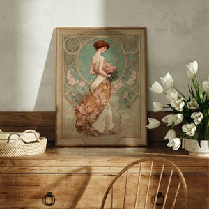 May include: An Art Nouveau style framed print featuring a woman in a flowing gown holding flowers. The print has a muted color palette with floral and geometric details. A woven tray and a vase of white tulips are on a wooden dresser.