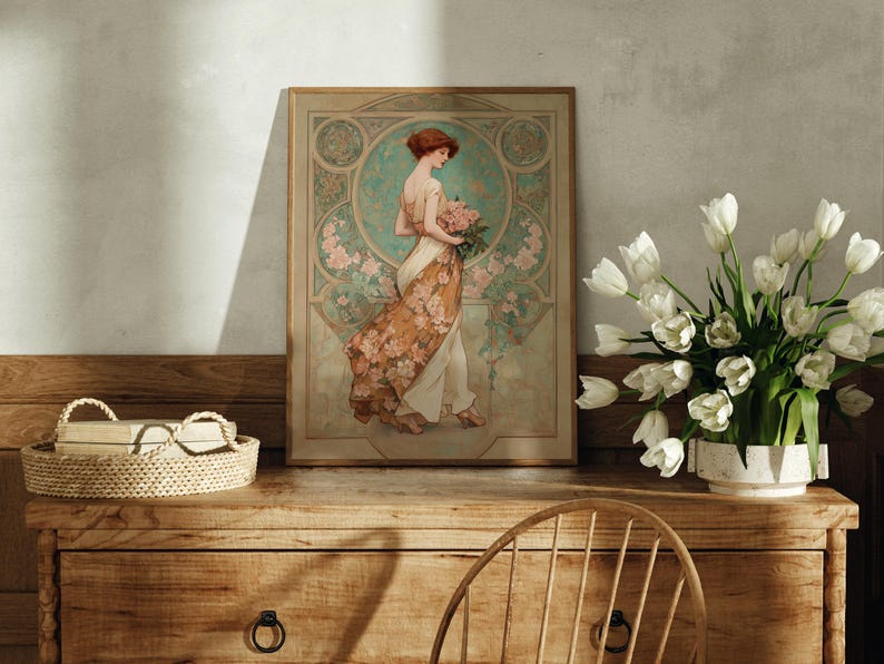 May include: An Art Nouveau style framed print featuring a woman in a flowing gown holding flowers. The print has a muted color palette with floral and geometric details. A woven tray and a vase of white tulips are on a wooden dresser.