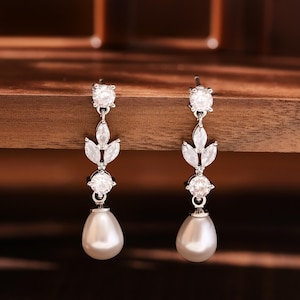 May include: A pair of silver earrings with a pearl drop and a leaf design with clear cubic zirconia stones.