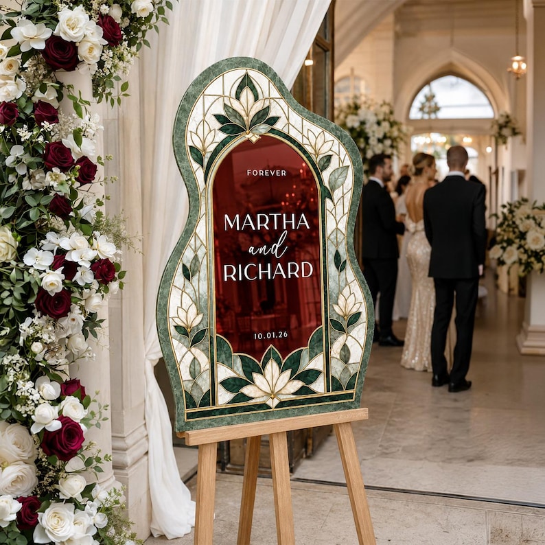 May include: A wedding welcome sign with a deep red center panel featuring the text FOREVER MARTHA and RICHARD 10.01.26. The sign has an arched top and is framed by a decorative border with green and white stained glass style floral patterns.