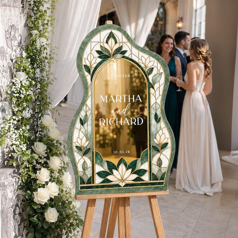 May include: An arched wedding sign with a green and white stained glass pattern border. The center features a gold reflective surface with the text "FOREVER MARTHA and RICHARD 10.01.26" printed in white. The sign is displayed on a wooden tripod easel.