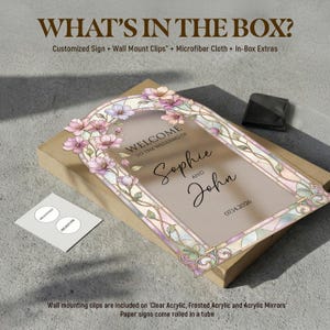 May include: A rectangular wedding sign featuring a stained glass-style floral border in pink and green tones. The text reads: WELCOME TO THE WEDDING OF Sophie AND John 07.14.2026. The sign is placed on a cardboard box with a small black pouch and a white card.