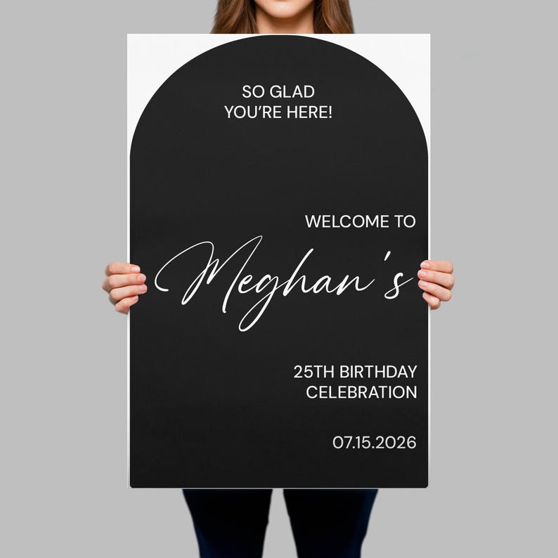 May include: A rectangular black sign with an arched top featuring white text that reads: SO GLAD YOU'RE HERE! WELCOME TO Meghan's 25TH BIRTHDAY CELEBRATION 07.15.2026. The sign has a modern, clean layout with a mix of sans-serif and script typography.