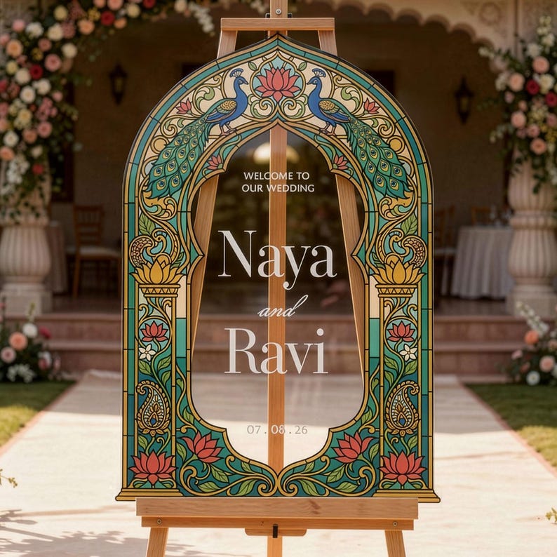 K&ouml;nnte beinhalten: Ein bogenf&ouml;rmiges Hochzeitsschild auf einer Holzstaffelei mit einem Rand im Buntglas-Stil, verziert mit Pfauen- und Lotusbl&uuml;tenmotiven. Der Text lautet: WELCOME TO OUR WEDDING, Naya and Ravi, 07.08.26. Das Design verwendet Blaugr&uuml;n-, Gold- und Rosat&ouml;ne.