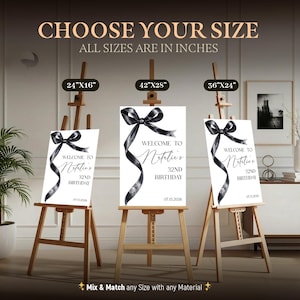 May include: Three white rectangular birthday signs on wooden easels, each featuring a black watercolor ribbon graphic and the text: Welcome to Natalie's 32nd Birthday 07.15.2026. Sizes labeled above are 24x16 inches, 42x28 inches, and 36x24 inches.