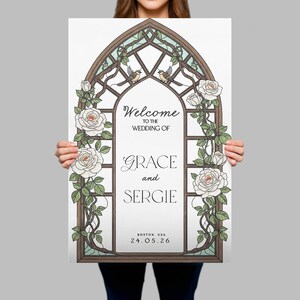 May include: A rectangular wedding sign featuring a brown arched frame resembling a stained glass window. The design includes white roses with green leaves and two small birds at the top. Text reads: Welcome to the wedding of Grace and Sergie, Boston, USA, 24.05.26.