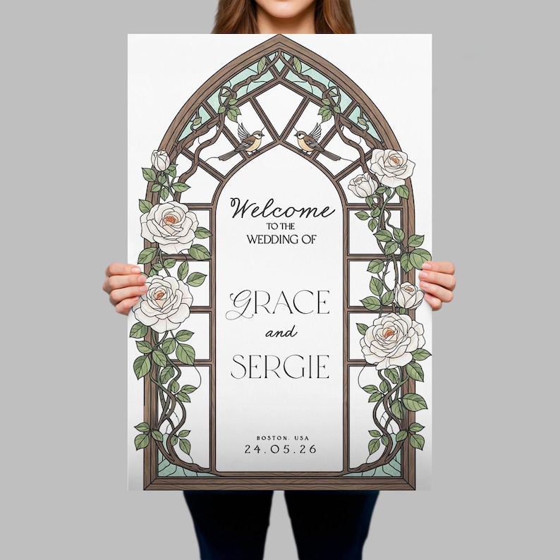 May include: A rectangular wedding sign featuring a brown arched frame resembling a stained glass window. The design includes white roses with green leaves and two small birds at the top. Text reads: Welcome to the wedding of Grace and Sergie, Boston, USA, 24.05.26.