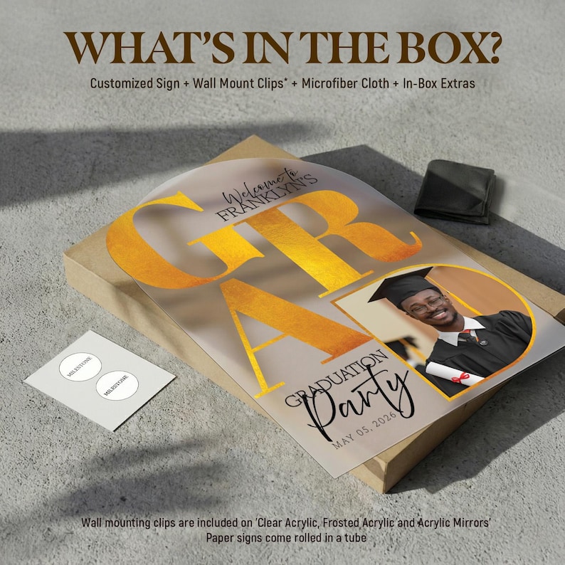 May include: A graduation party sign with the word "GRAD" in gold lettering. The sign includes a photo of a graduate and the text "Graduation Party May 05, 2026". The box includes wall mount clips and a microfiber cloth.