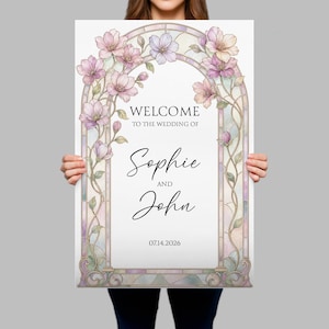 May include: A rectangular wedding welcome sign featuring a stained glass archway frame with pastel pink and purple flowers. The text reads: WELCOME TO THE WEDDING OF Sophie AND John 14.07.2026. The design includes intricate glass panel details.