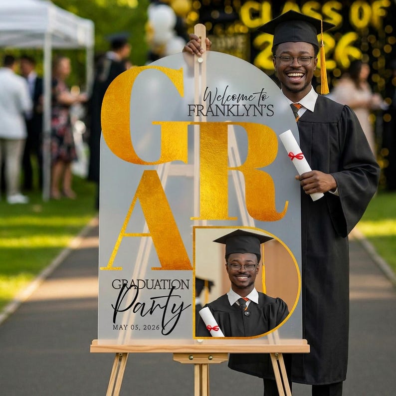 May include: A graduation party sign with gold lettering that reads "GRADUATION PARTY" and "Welcome to Franklyn's". The sign is held by a graduate in a cap and gown, holding a diploma. The date "MAY 05, 2026" is also displayed.