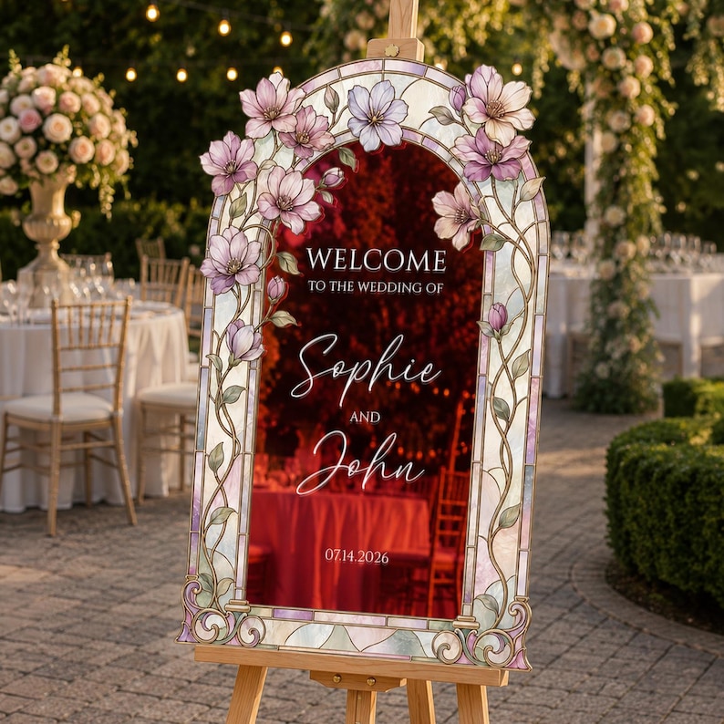 May include: An arched wedding welcome sign featuring a stained glass border with pink and purple floral accents. The centre displays the text: WELCOME TO THE WEDDING OF Sophie AND John 07.14.2026. The sign is mounted on a wooden easel stand.