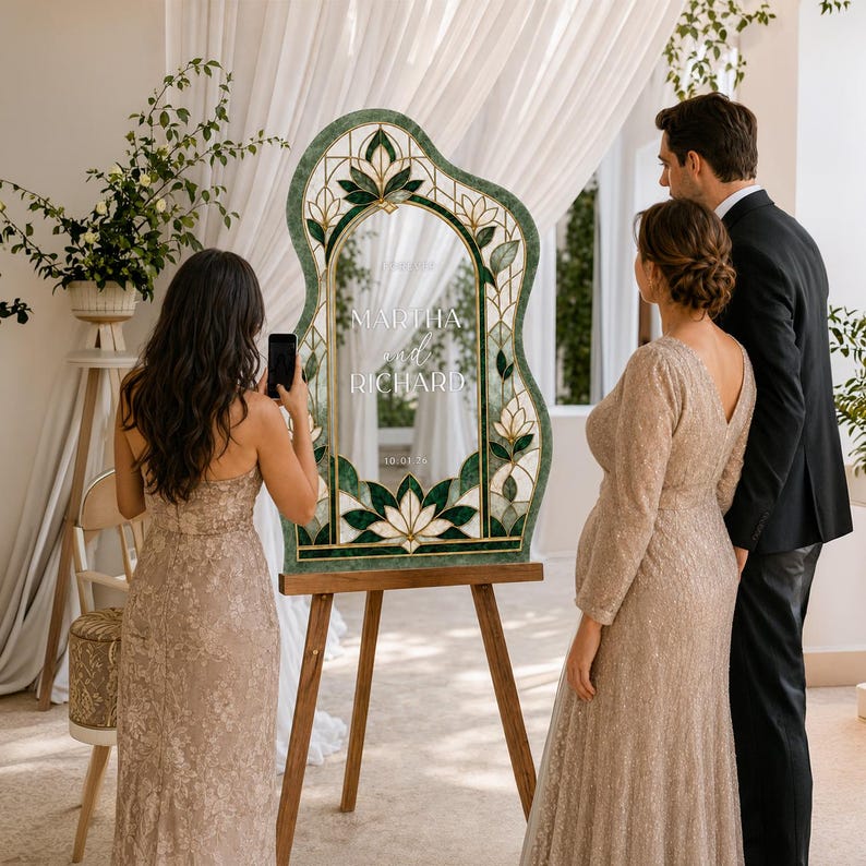 May include: An arched wedding sign with a green stained glass border featuring floral motifs. The center is clear with white text reading MARTHA and RICHARD and the date 10.01.26. The sign is displayed on a wooden tripod easel stand.