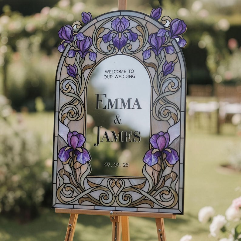 May include: An arched wedding welcome sign featuring a stained glass border with purple iris flowers and gold scrollwork. The center mirror displays the text: WELCOME TO OUR WEDDING, EMMA & JAMES, and 07.03.26 in a dark serif font.