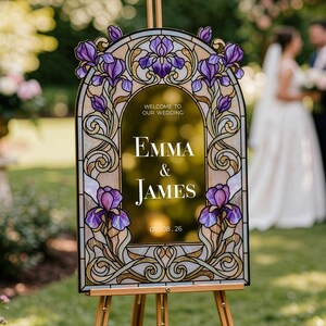 May include: An arched wedding welcome sign featuring a stained glass style border with purple iris flowers and gold scrollwork. The center text reads: Welcome to our wedding, Emma & James, 07.08.26. The sign is displayed on a wooden easel.