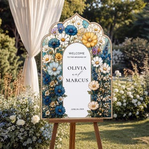May include: An arched wedding welcome sign featuring a stained glass-style floral border with blue, yellow, and white flowers. The center white panel displays the text: WELCOME TO THE WEDDING OF OLIVIA and MARCUS JUNE 24, 2026 in black lettering.