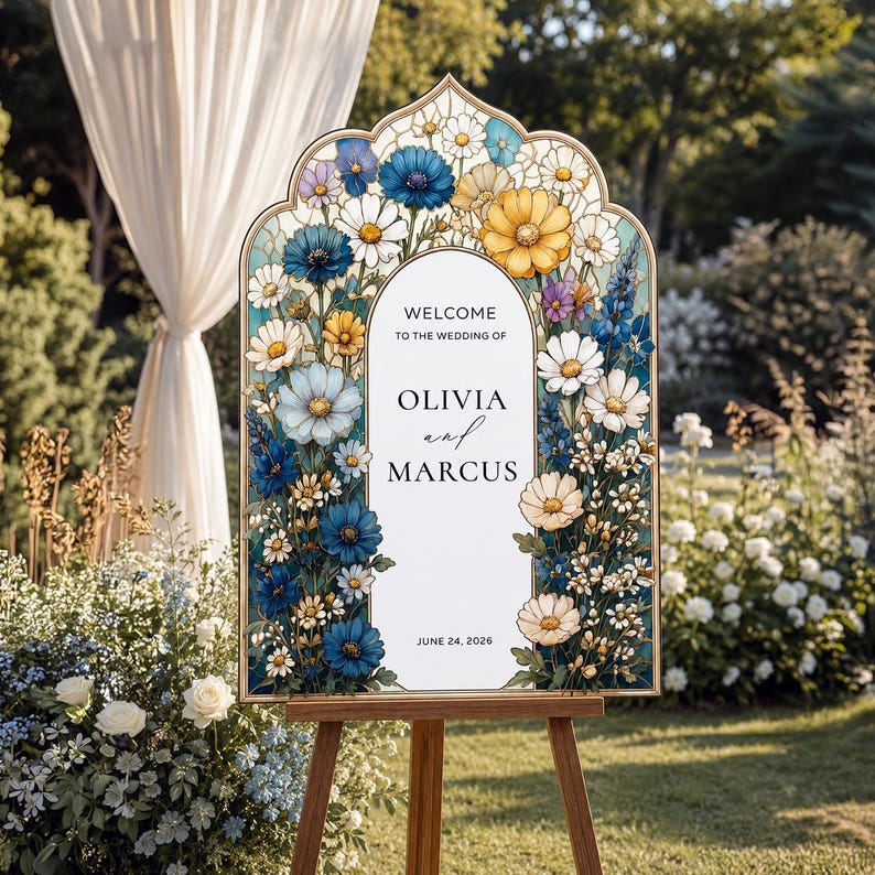 May include: An arched wedding welcome sign featuring a stained glass-style floral border with blue, yellow, and white flowers. The center white panel displays the text: WELCOME TO THE WEDDING OF OLIVIA and MARCUS JUNE 24, 2026 in black lettering.