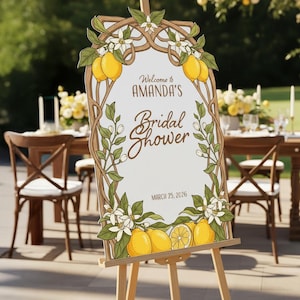 May include: A wooden easel displays a sign for Amanda's Bridal Shower, March 25, 2026. The sign features a lemon and floral design with the words "Welcome to Amanda's Bridal Shower". The sign is decorated with lemons, white flowers, and green leaves.