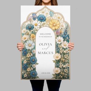 May include: A rectangular wedding welcome sign featuring a decorative archway frame filled with illustrations of blue, yellow, and white flowers. The center text reads: WELCOME TO THE WEDDING OF OLIVIA and MARCUS JUNE 24, 2026, in black serif and script fonts.