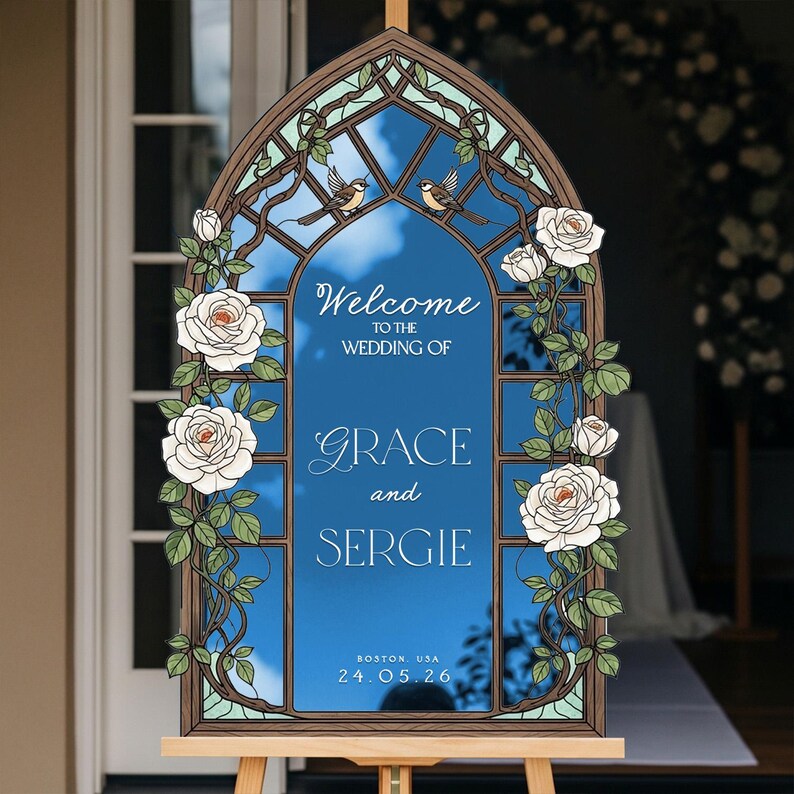 May include: An arched wedding welcome sign featuring a stained glass window design with white roses, green leaves, and two small birds. The blue center panel displays the text: Welcome to the wedding of Grace and Sergie, Boston, USA, 24.05.26.