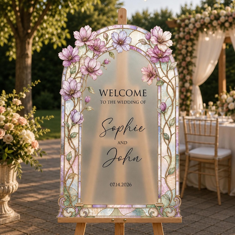 May include: An arched wedding welcome sign featuring a frosted centre panel with the text Welcome to the wedding of Sophie and John 07.14.2026. The frame is decorated with stained glass style pink magnolia flowers and green vines.