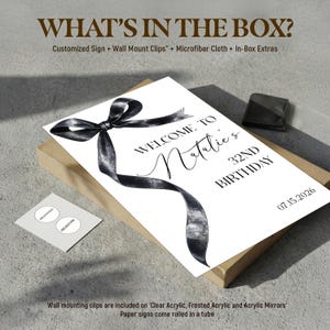 May include: A rectangular sign featuring a black watercolor-style ribbon graphic and the text: WHAT'S IN THE BOX? Customized Sign + Wall Mount Clips + Microfiber Cloth + In-Box Extras. WELCOME TO Natalie's 32ND BIRTHDAY 07.15.2026. Includes a small card.