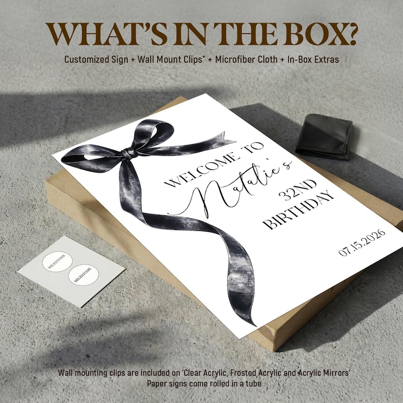 May include: A rectangular sign featuring a black watercolor-style ribbon graphic and the text: WHAT'S IN THE BOX? Customized Sign + Wall Mount Clips + Microfiber Cloth + In-Box Extras. WELCOME TO Natalie's 32ND BIRTHDAY 07.15.2026. Includes a small card.