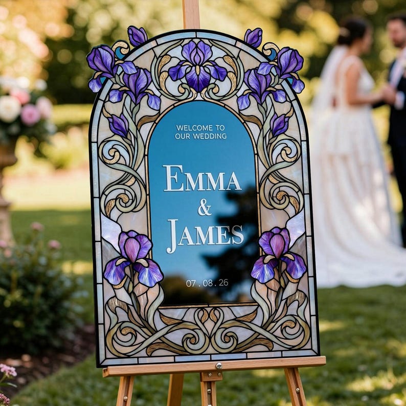 May include: An arched wedding welcome sign featuring a stained glass-style border with purple iris flowers and gold scrollwork. The center is a blue panel with the white text: WELCOME TO OUR WEDDING, EMMA & JAMES, 07.08.26, displayed on a wooden easel.